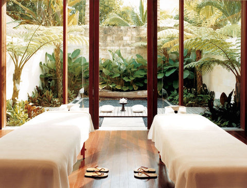 Two massage beds in a room overlooking a plunge pool and palm trees.