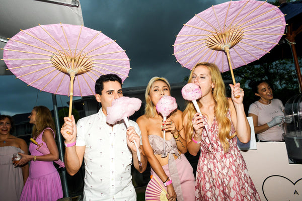 Party goers holding pink parasols and eating cotton candy
