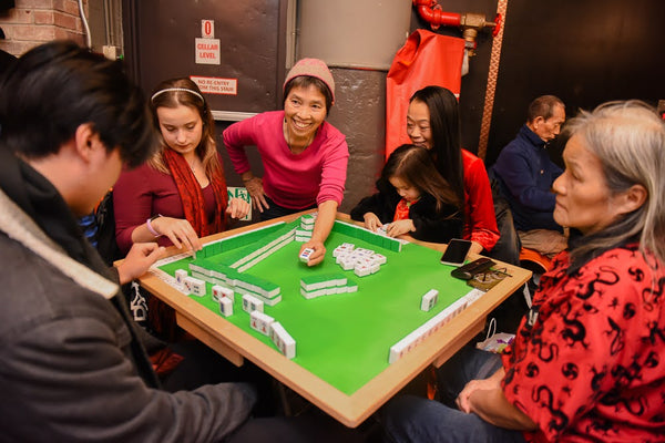 People playing mahjong with woman instructing