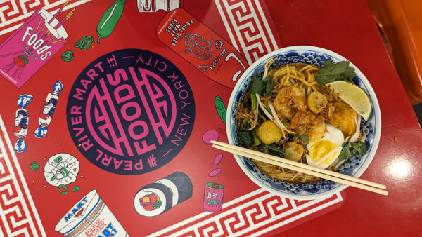 Bowl of laksa noodles on table with Pearl River mart foods logo and food design