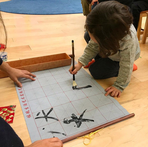 Child practicing Chinese calligraphy with a reusable set