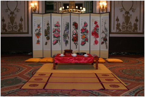 Screen with Asian design in front of low table and pillows set up for traditional Chinese and Korean tea ceremony