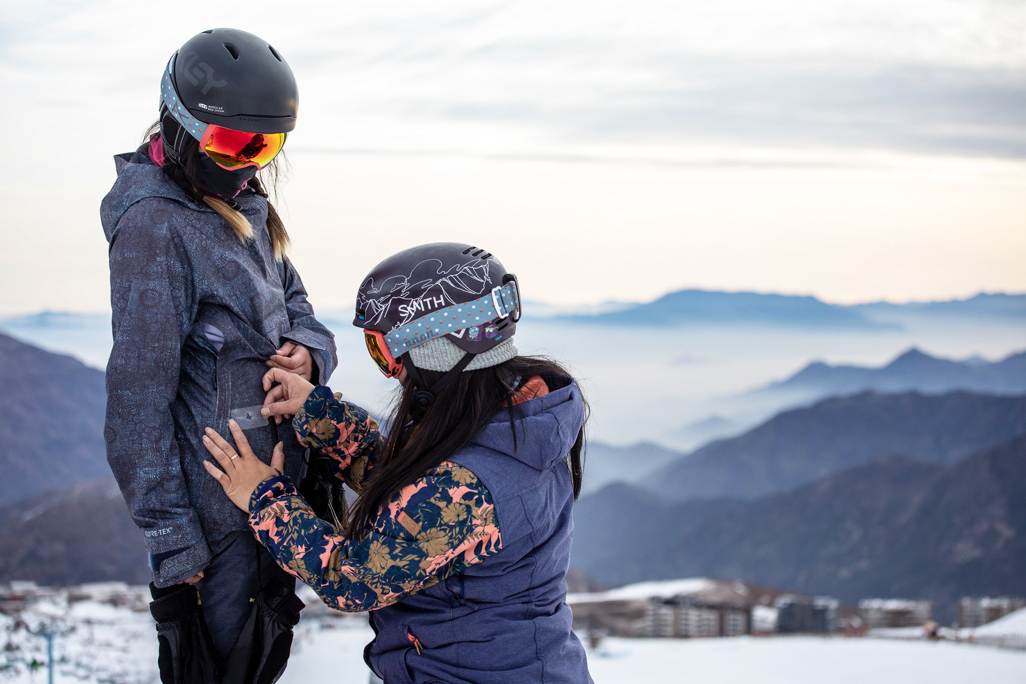 Two skiiers on a slope, one skiier is putting a GEAR AID mini patch on the other skiier's jacket