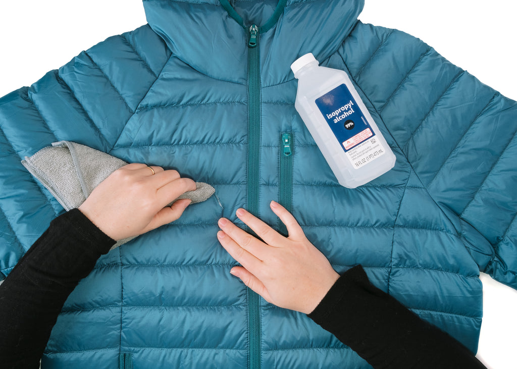 Down jacket being cleaned by two hands with IPA on a white background