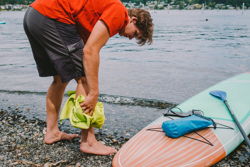 GEAR AID Microfiber towel being used to dry off a man's leg next to a body of water and his paddleboard