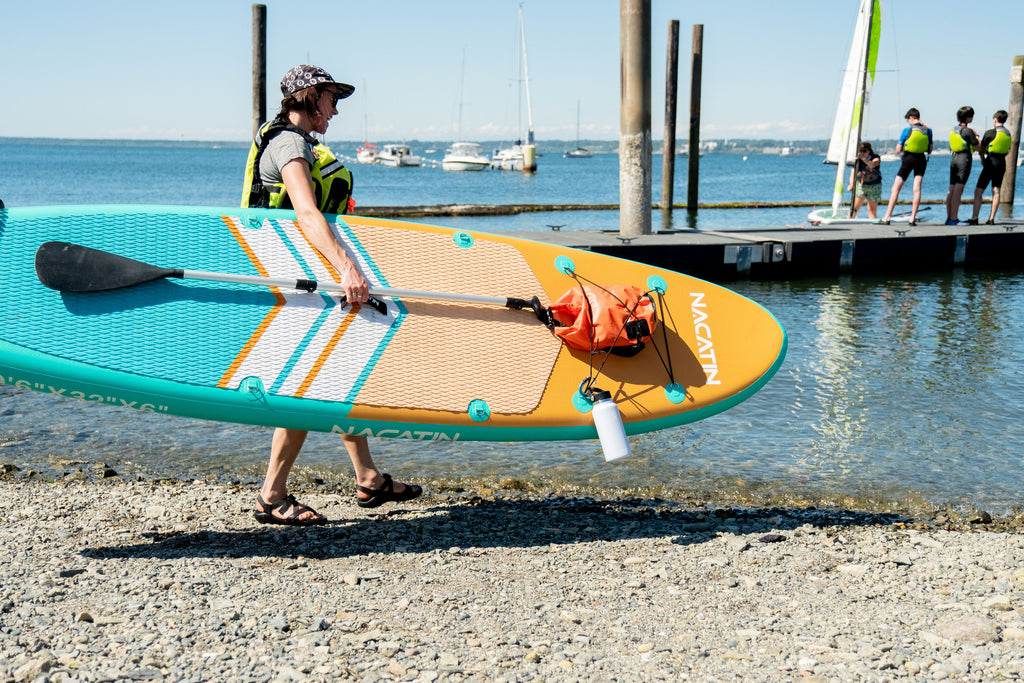 Woman carrying SUP to water past a dock