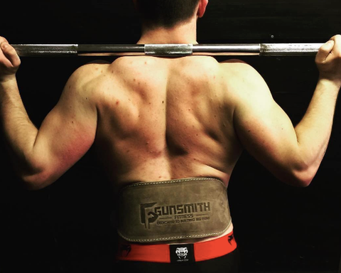 athlete standing confidently with a barbell over their shoulders, showcasing the Gunsmith Fitness Shibusa weightlifting belt as both a fashion statement and essential support during weightlifting.