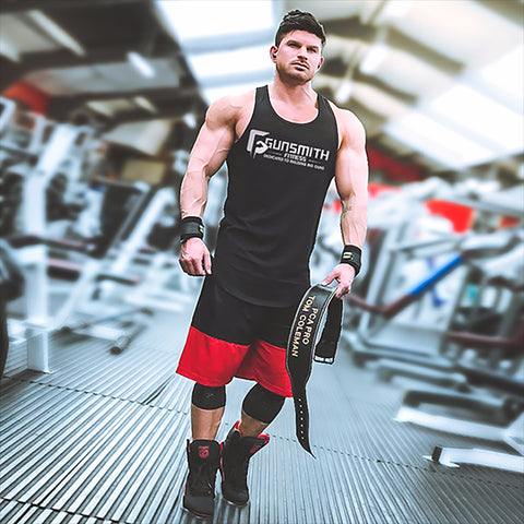 Tom Coleman showcasing strength and dedication in a gym, sporting a Gunsmith tank top while confidently holding a customised weight lifting belt.