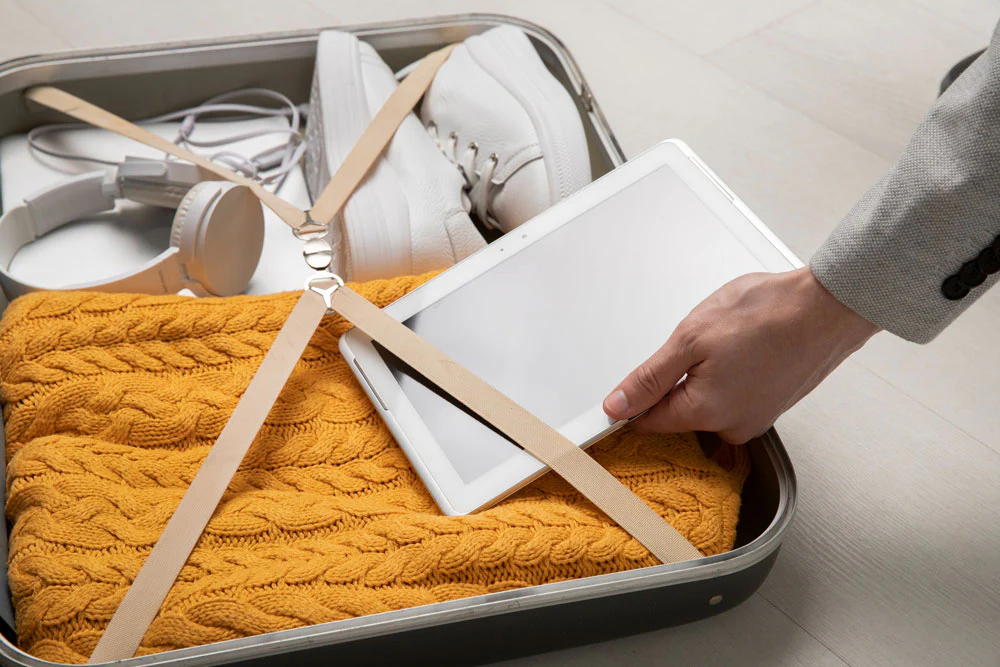 A traveller adds their laptop to the top of their luggage