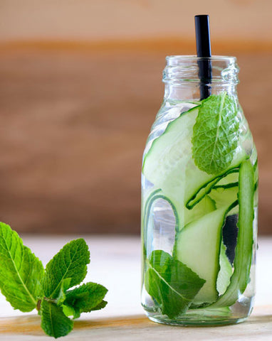 an image of a virgin Cucumber Mint Spritzer. Fresh mint leaves are sitting next to the cup and there is a black straw inserted into the top of the cup