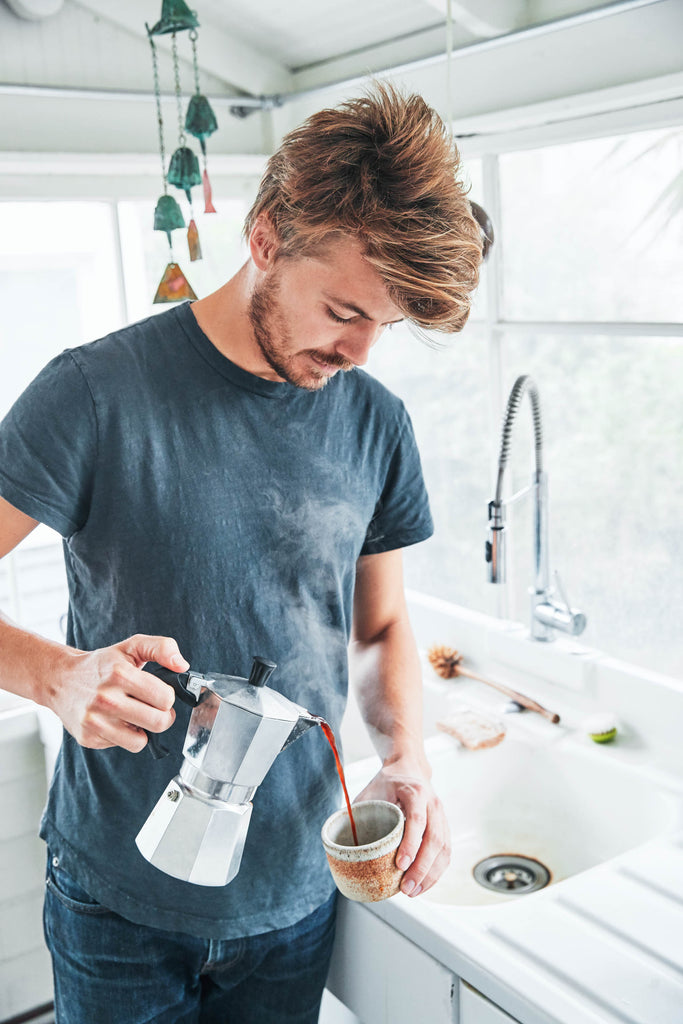 Homemade espresso being poured from an Italian moka pot into a ceramic mug by Casey Wojtalewicz, co-founder of Canyon Coffee, in a bright natural lit white kitchen.