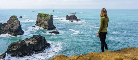 Model standing on top of a cliff looking out at water