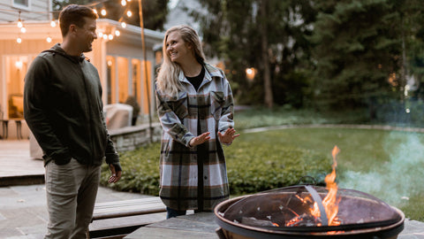 Couple wearing Woolx clothing, smiling and standing by firepit outside