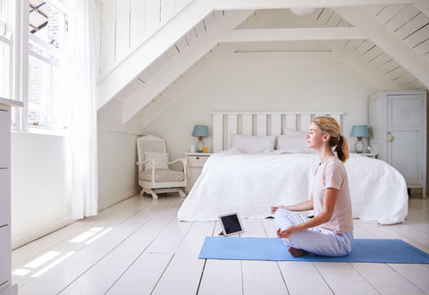 Ragazza che fa yoga sul tappetino yoga blu in camera da letto bianca