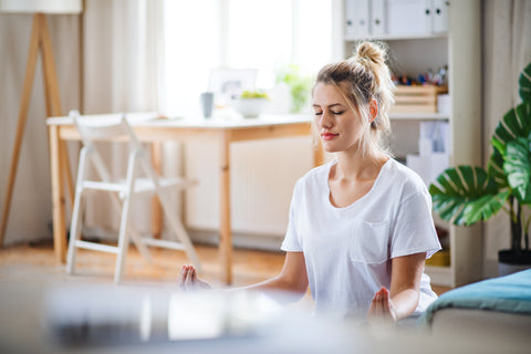Mujer con una camiseta blanca meditando en casa