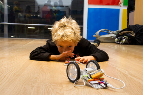 Kid laying on the floor controlling his robot car invention.