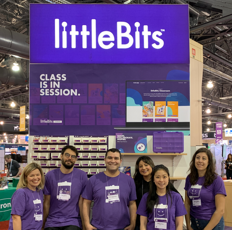 Group of people smiling wearing matching purple littleBits tshirts, smiling in front of a trade show booth.