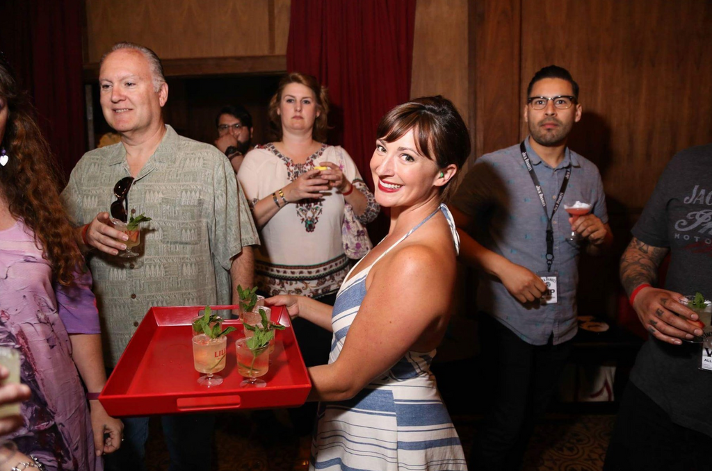 woman in a striped dress holding a tray of drinks in a crowded bar