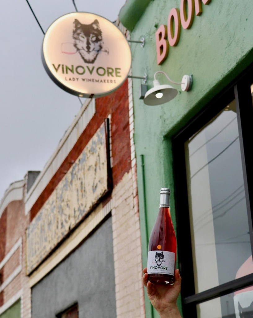 exterior of a wine shop with a hand holding a wine bottle in the foreground