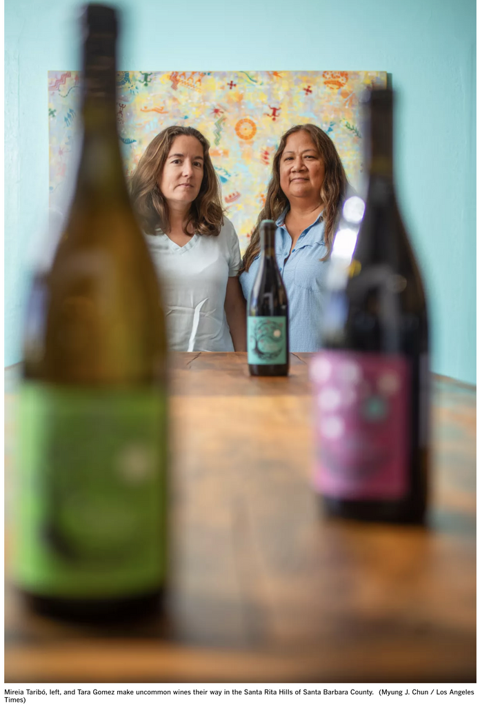 two women in the background, with bottles of wine in the foreground