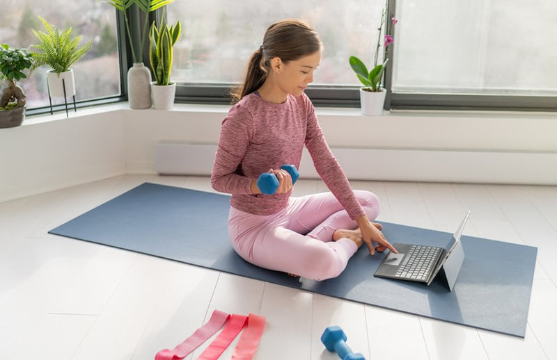 a woman working out with DMoose neoprene dumbbell while using the laptop