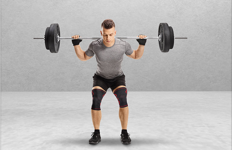 A man doing squat while holding weighted barbell behing his neck while wearing DMoose knee sleeves