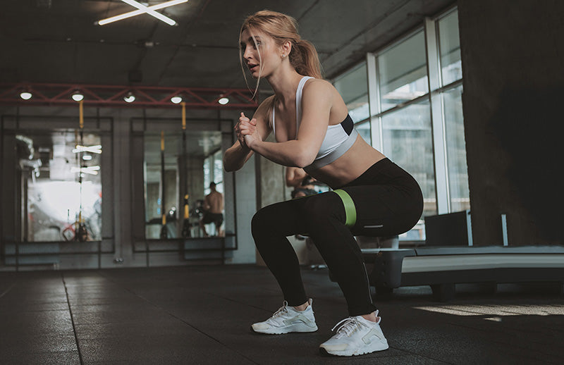 A woman doing squat with wearing DMoose resistance band on her thighs