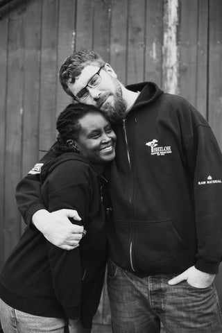 Black and white picture of husband and wife team Mark and Jean Armstrong wearing Shiloh-branded hoodies, standing with an arm around each other and smiling