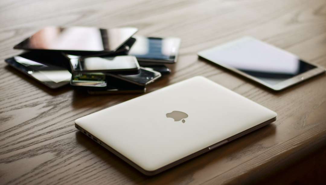 A pile of devices stacked on top of each other with an Apple laptop in front.