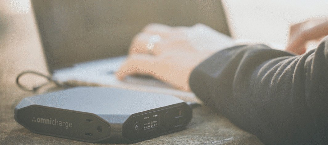 An Omnicharge power pack charging a laptop as someone works on it.