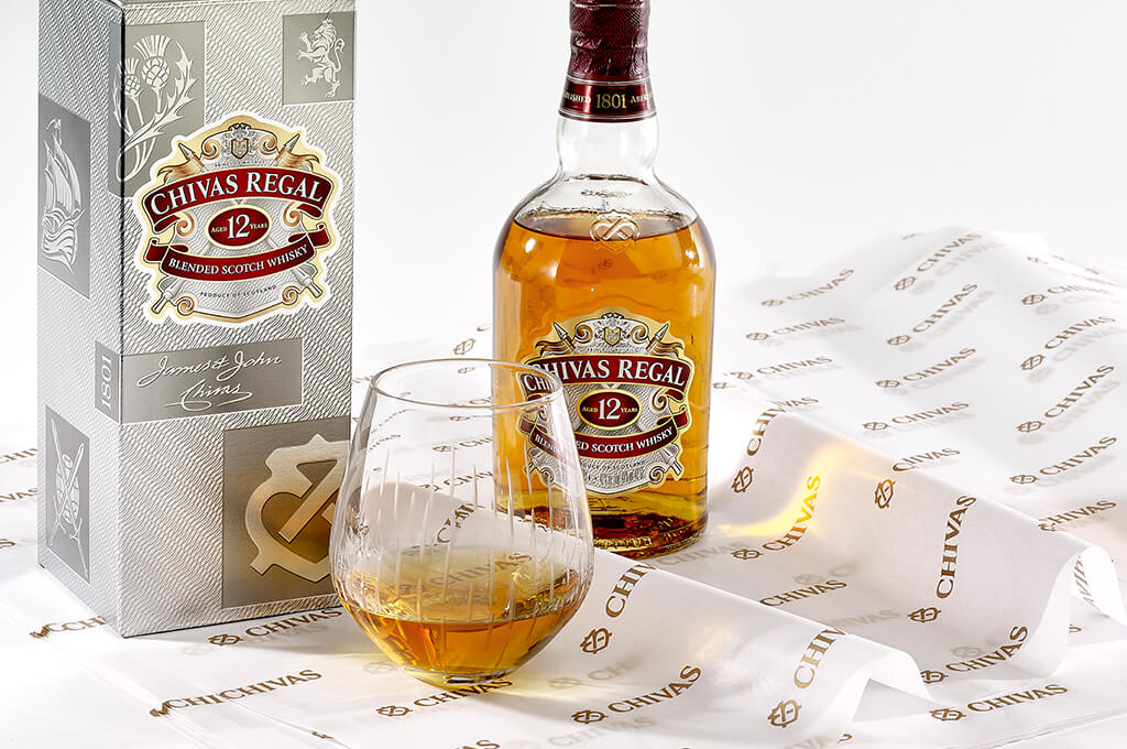 A bottle of Chivas regal expertly displayed on custom printed Chivas tissue paper for gift packaging that works to elevate the unboxing experience