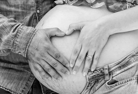 Man and woman's hands making a heart on her pregnant belly