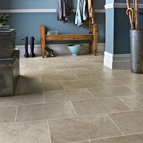 A stylish entryway featuring light tile flooring, a wooden bench, rain boots, and a blue bowl against a blue wall with hanging coats.