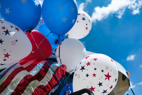 A gathering of 4th of July themed balloons flying in the sky with the American Flag.