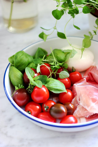 A bowl filled with fresh basil, cherry tomatoes, proscuitto, and mozarella cheese.