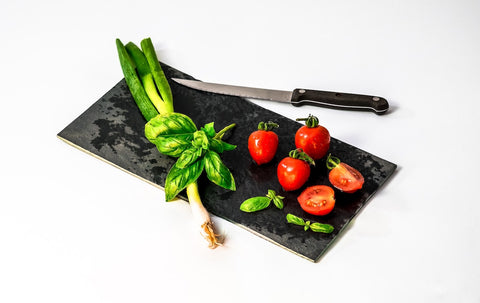 A cutting board with cherry tomatoes, basil, and a kitchen knife.