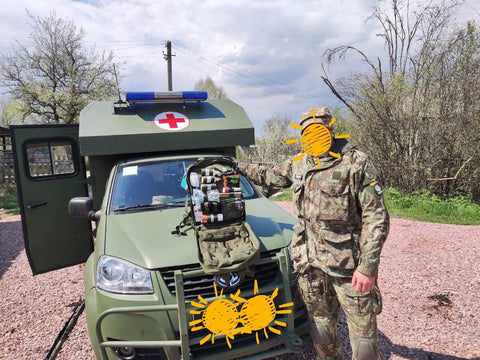 An image of a soldier standing in front of a military medical car with his Sunflower of Peace backpack.
