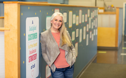 Michelle Brandriss, Name Bubbles founder and president, standing and smiling in front of a colorful classroom wall.