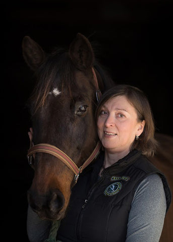 a dark bay horse and a woman standing before dark background