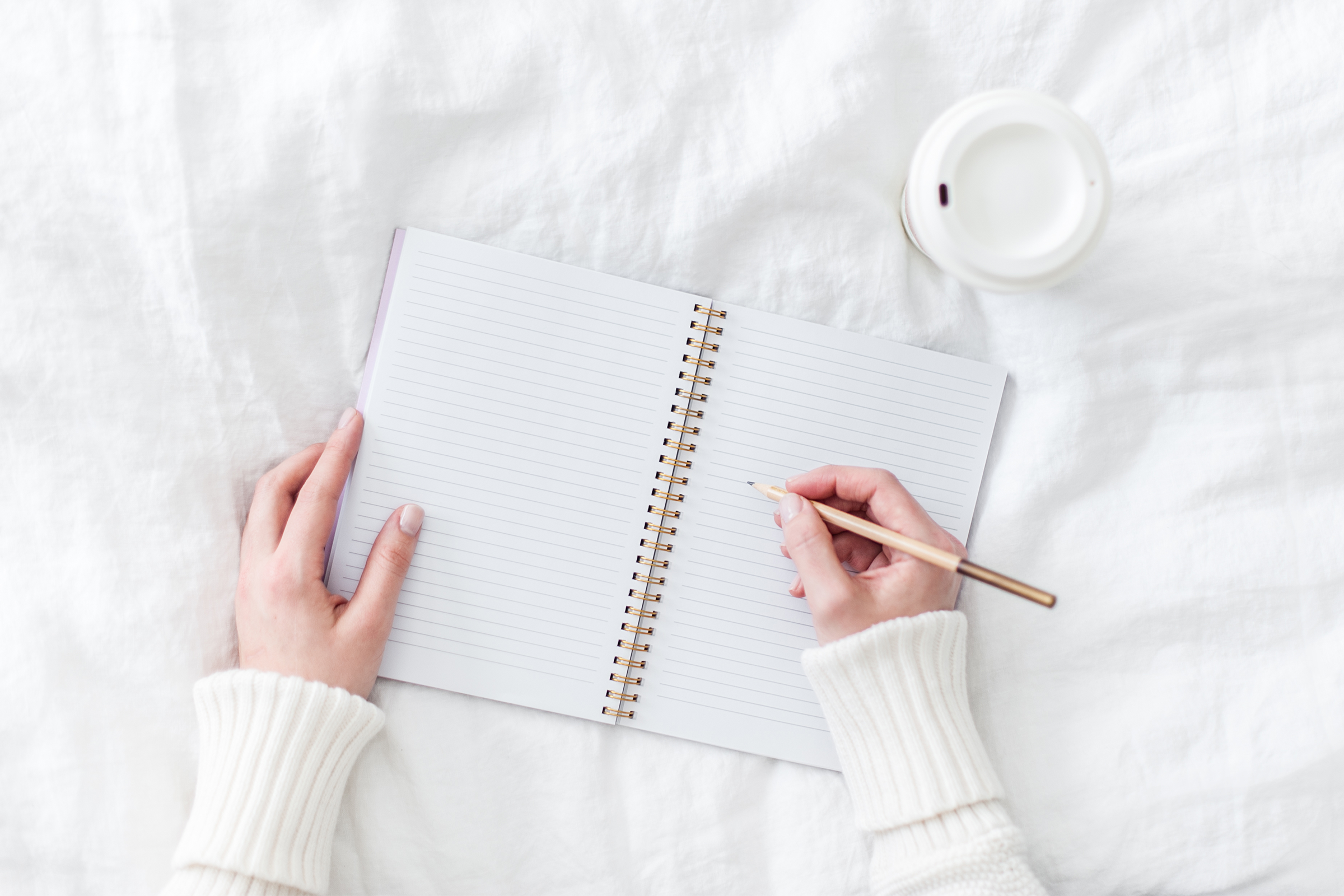 A woman's hand writing in a notebook next to a cup of coffee