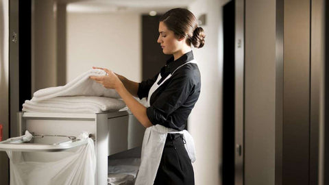 7 Ways to Tell if Your Hotel Room is Really Clean - A hotel cleaner in uniform examining white sheets