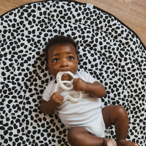 a baby chewing on the etta loves logo teether on an animal print playmat