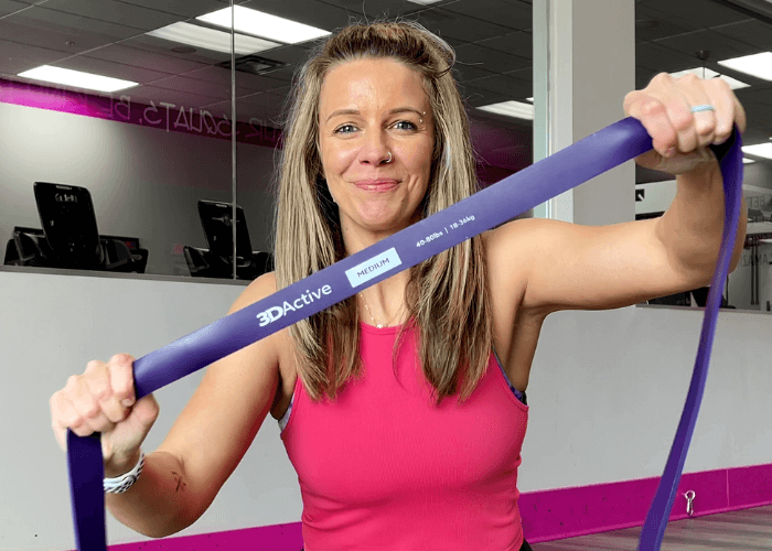 Woman holding stretched purple power band to camera.