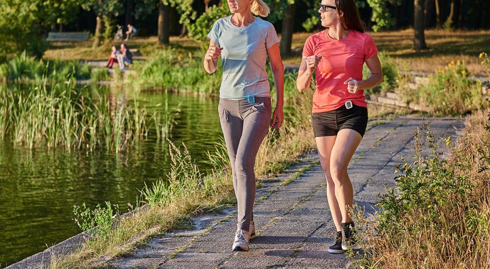 Two young women walking outdoors wearing a simple step counter on their waist to track steps