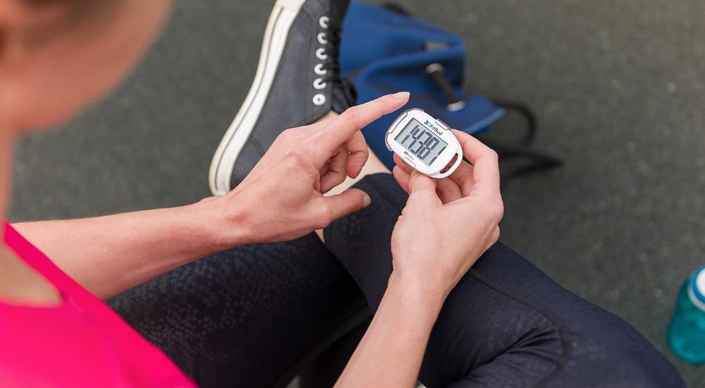 Woman holding 3DFitBud Pedometer and looking at screen display which reads 14 thousand recorded steps