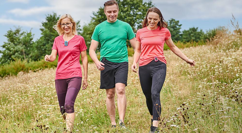 Two women and a man walking outdoors in a field using 3DFitBud Pedometers to count their steps