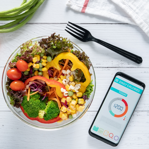 Phone with a calorie tracking app open next to a salad bowl