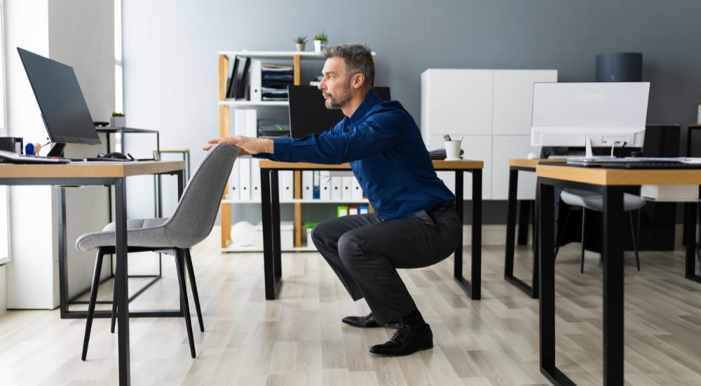Man squatting with the help of chair at his office desk