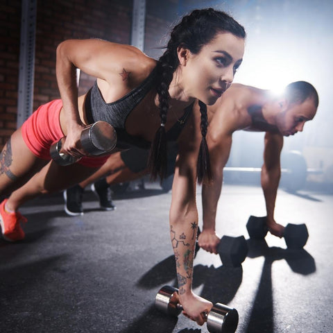 Woman and man warming up for CrossFit workout. Push ups with dumbbells
