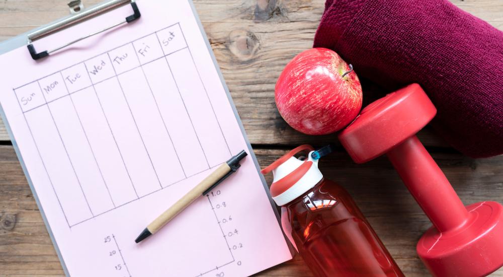 Workout weekly planner next to water bottle and red apples